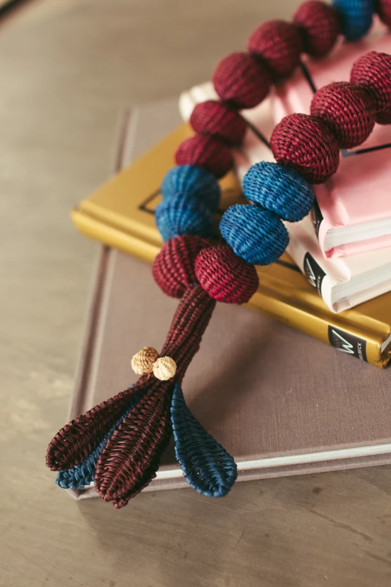 Primer plano de pulsera artesanal con cuentas tejidas burdeos y azul con borlas dobles – Areito Gallery