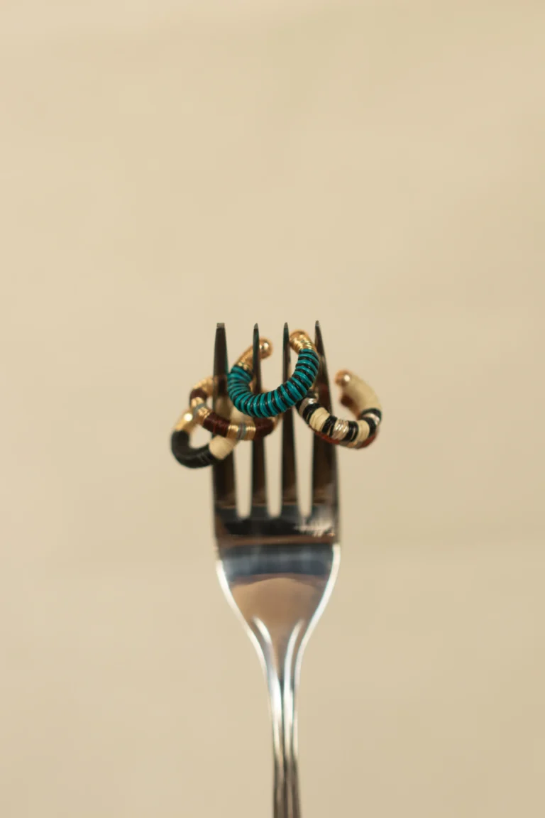 Aretes artesanales turquesa y dorado exhibidos creativamente en tenedor plateado – Areito Gallery