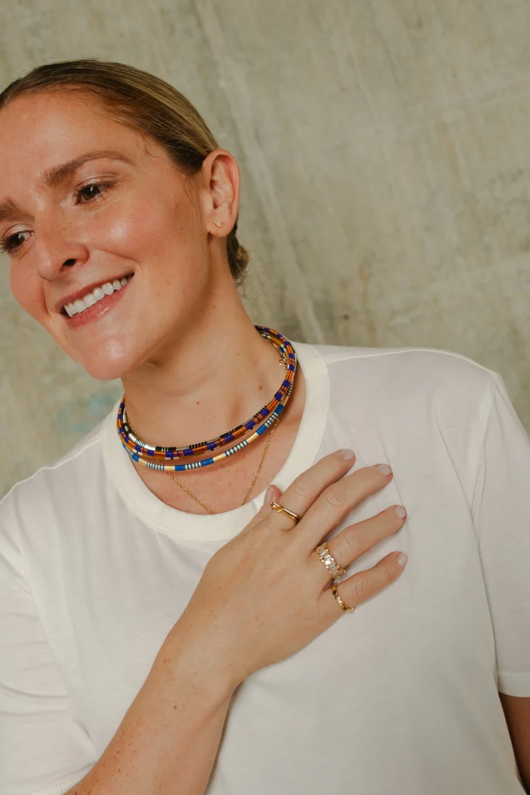 Modelo sonriente con collar artesanal de cuentas multicolor azul y naranja con cadena dorada – Areito Gallery